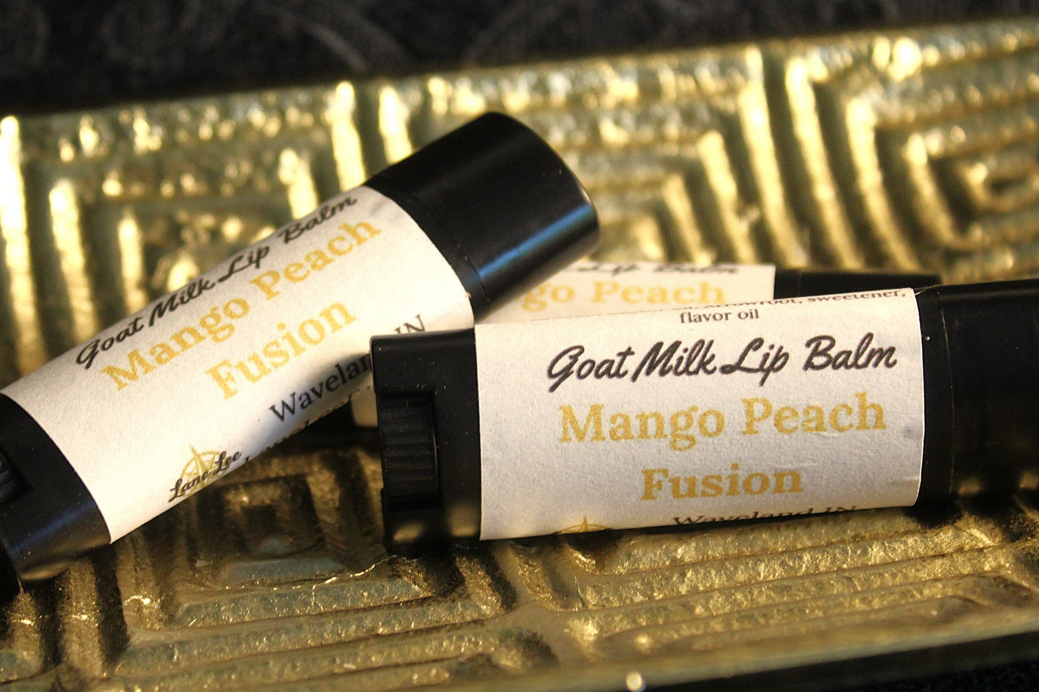 Two goat milk lip balms labeled 'Mango Peach Fusion' on a decorative gold tray.